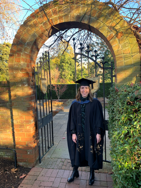 Anna Damoli under a brick arch at University of Reading, wearing her graduation gown.